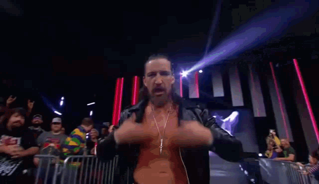 a wrestler in a black leather jacket adjusts his ear buds in front of a crowd .