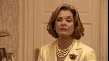 a woman wearing a yellow suit and pearls is sitting in a chair .