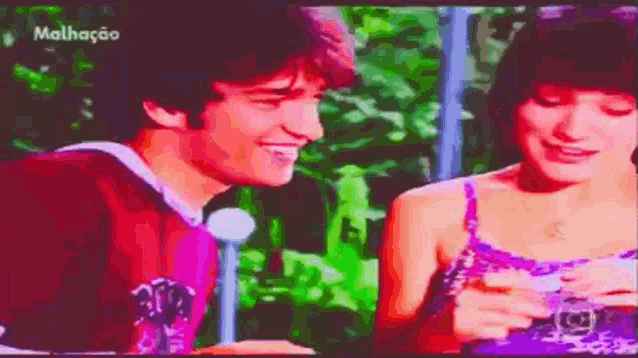 a man and a woman are sitting next to each other and smiling with the word malhacao on the bottom right