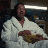 a man in a robe is sitting in a chair eating popcorn .