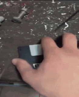 a close up of a person 's hand holding a floppy disk with the letter f on it