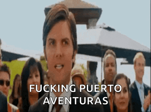 a man in a suit and tie stands in front of a crowd of people and says fucking puerto aventuras .