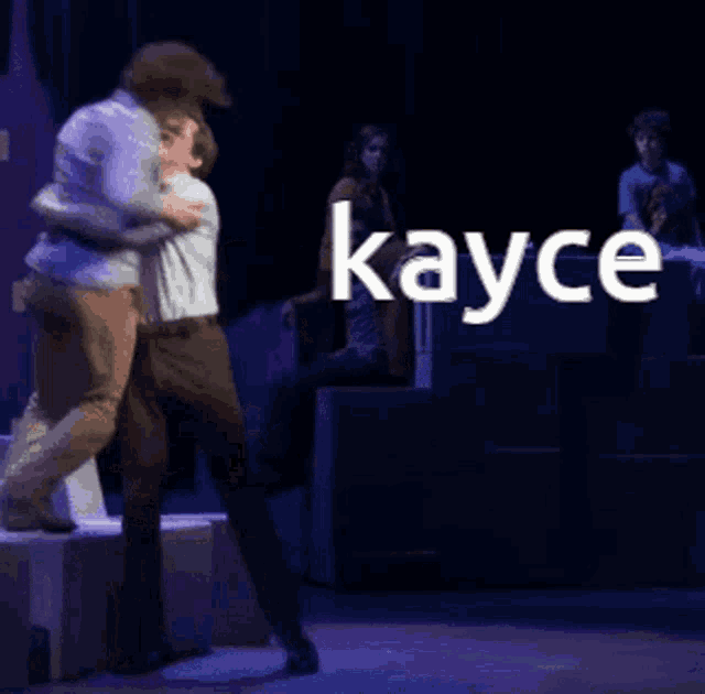 two men are hugging on a stage with the word kayce in the corner