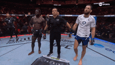 a man in a white ufc shirt stands next to a referee