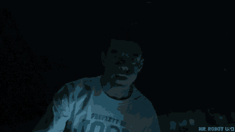 a man in a white shirt is sitting in the dark looking at something .