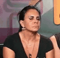 a woman wearing a black shirt and earrings is sitting in front of a purple wall .