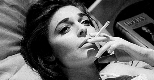 a woman is smoking a cigarette while laying in bed .