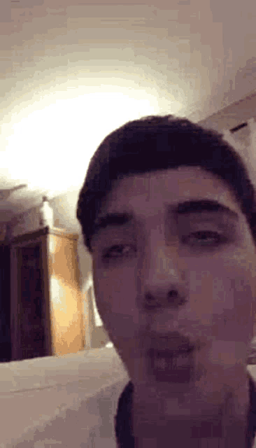 a young man is making a funny face while sitting on a bed in a room .