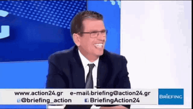 a man in a suit and tie is laughing in front of a briefing sign