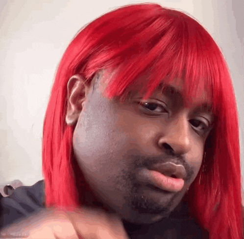 a man wearing a red wig and a black shirt is making a funny face