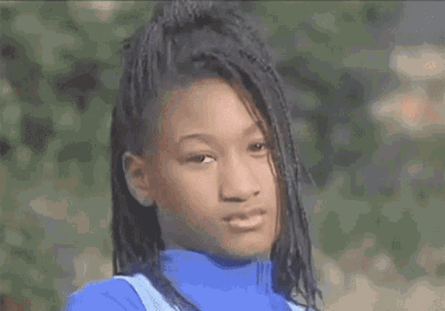 a young girl with braids is wearing a blue turtleneck sweater and looking at the camera .