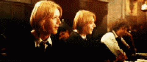 two boys with red hair are sitting at a table in a dark room with other people .