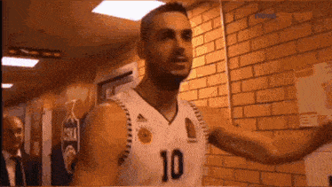 a basketball player with the number 10 on his jersey is standing in front of a brick wall