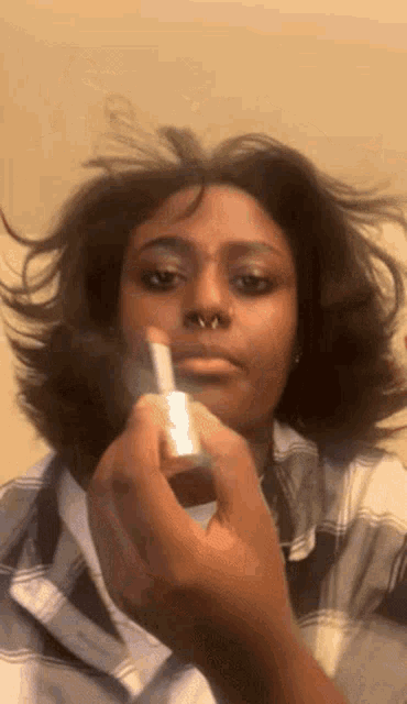 a woman with a nose ring is applying lipstick to her lips