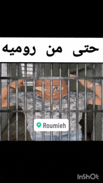 a man is behind bars in a jail cell with roumieh in the corner .