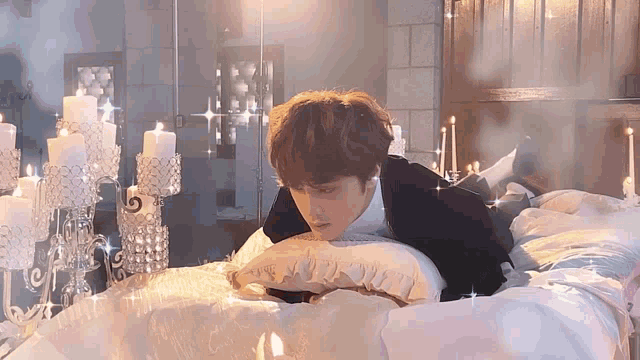 a man in a black suit is laying on a bed with a pillow and candles .