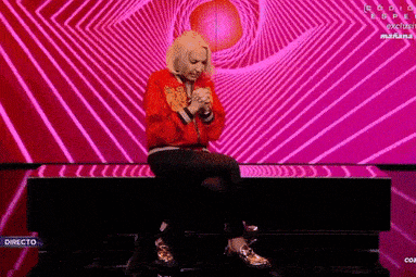 a woman in a red jacket is sitting in front of a pink background .