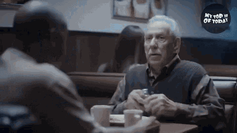 two men are sitting at a table in a diner talking .