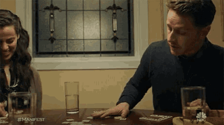a man and a woman are playing a game of cards with the hashtag #manifest on the bottom