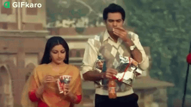 a man and a woman are standing next to each other eating snacks .