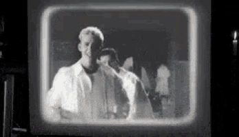 a black and white photo of a man standing in front of a mirror .