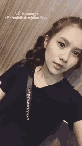 a woman wearing a black shirt with a strap that says ' nikon ' on it is taking a selfie