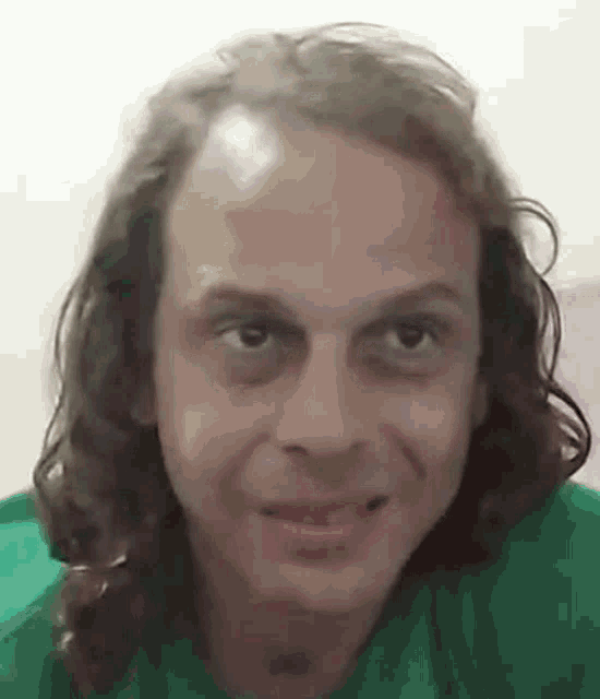 a man with long hair is smiling and looking at the camera .