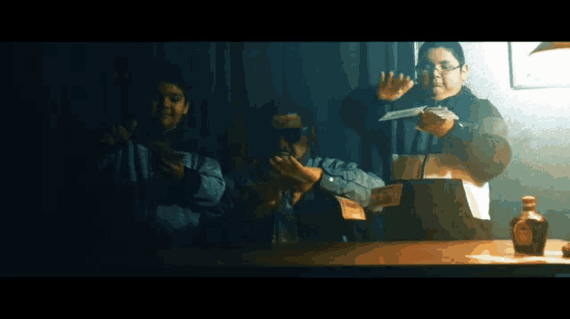 a group of people standing around a table with a bottle of whiskey in the foreground