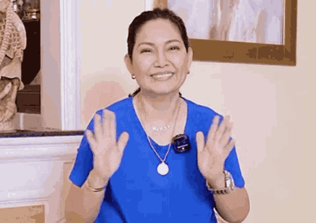 a woman wearing a blue shirt and a necklace is waving her hands in a living room .