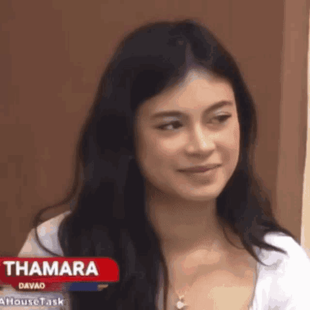 a woman with long black hair is smiling and looking at the camera while wearing a white shirt .
