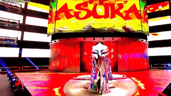 a woman in a kimono is standing on a stage in front of a large screen that says asura .