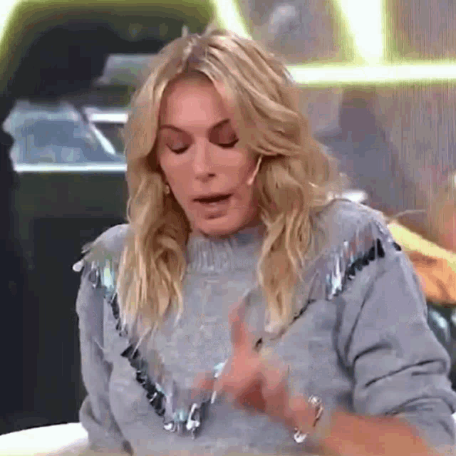 a woman with blonde hair is wearing a gray sweater and making a face .