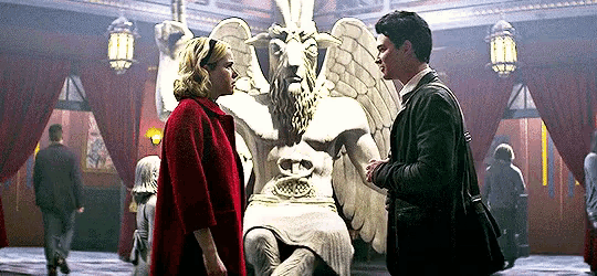 a man and a woman are standing next to a statue of a goat with wings .