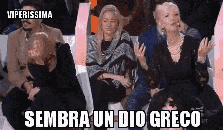 a group of people are sitting in a row with the words sembra un dio greco written on the screen .