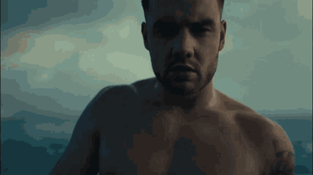 a shirtless man with a tattoo on his arm is standing in front of the ocean .