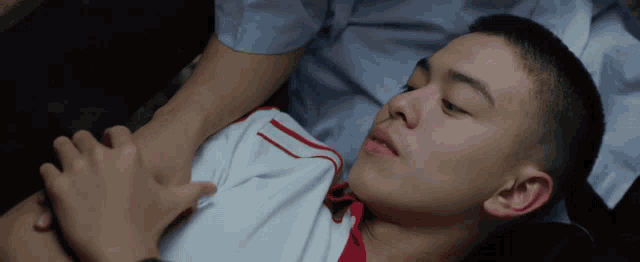 a man in a white shirt with red stripes is laying on a bed