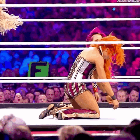 a woman is kneeling in a wrestling ring in front of a crowd with the letter f in the background .