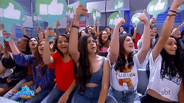 a group of young women are sitting in a stadium holding up thumbs up signs .