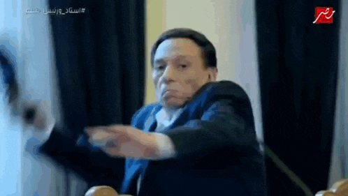 a man in a suit and tie is making a funny face while sitting in a chair .