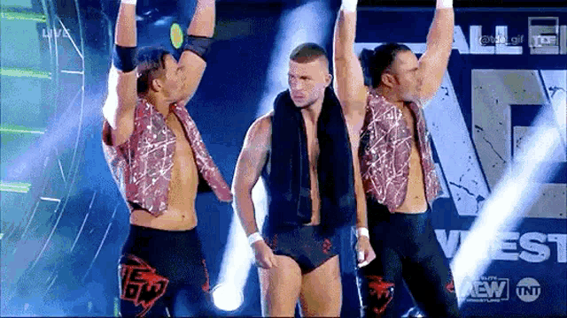 three wrestlers are standing on a stage holding their arms in the air .