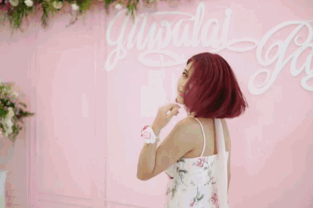 a woman with red hair is standing in front of a pink wall with flowers