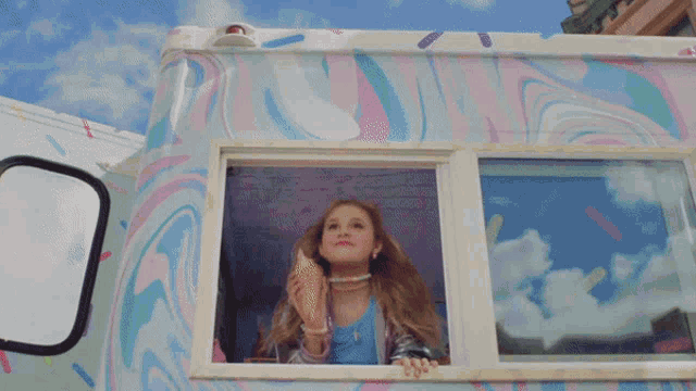 a girl eating an ice cream cone while looking out of an ice cream truck window