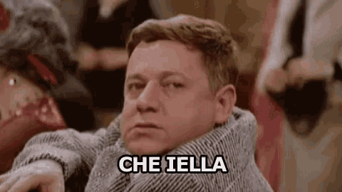 a man is sitting in a chair with a scarf around his neck and the words `` che iella '' written on his face .