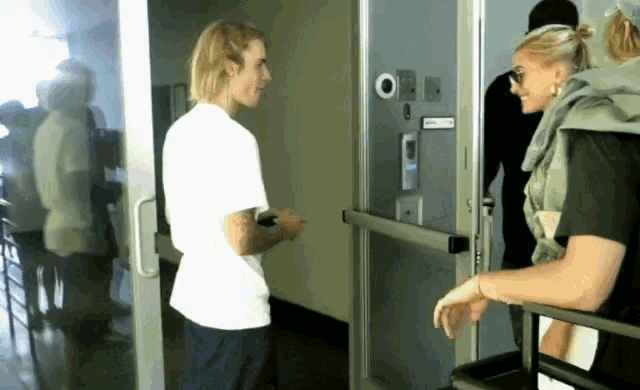 a man in a white shirt is talking to a woman in a black shirt in a hallway .