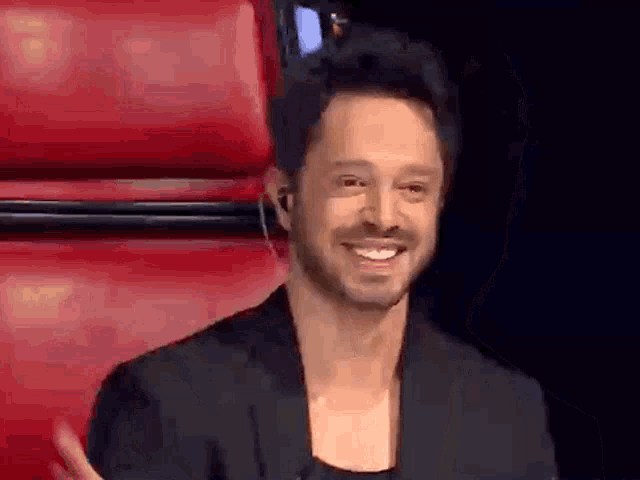 a man with a beard is smiling in a red chair .