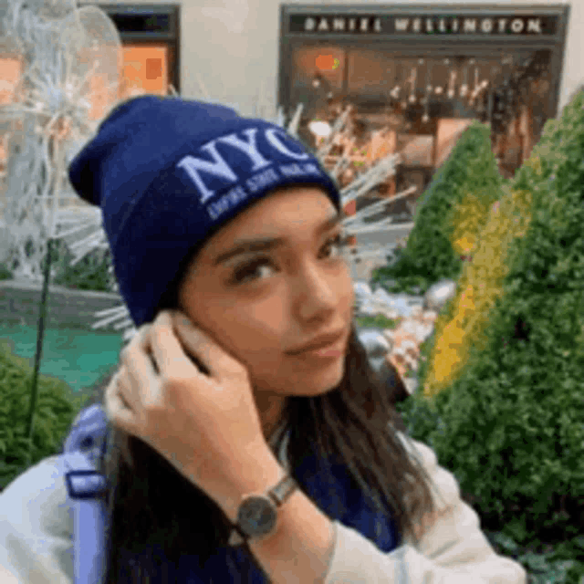 a woman wearing a blue nyc beanie talking on a cell phone .