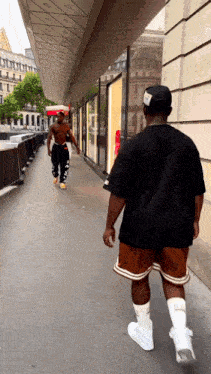 a man in a black shirt and brown shorts is walking down the sidewalk