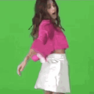 a little girl in a pink jacket and green skirt is dancing in front of a white box .