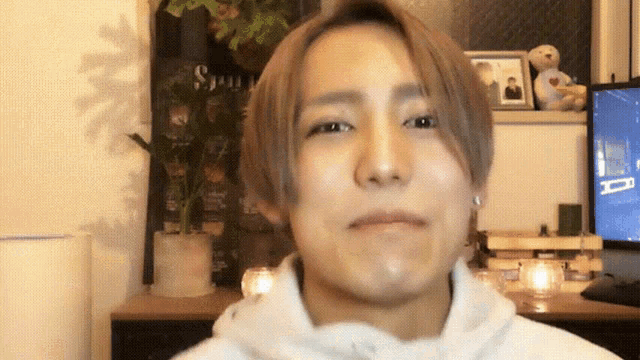 a man in a white hoodie looks at the camera with a sign in the background that says ' spring '