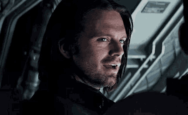 a man with long hair and a beard is looking at the camera .